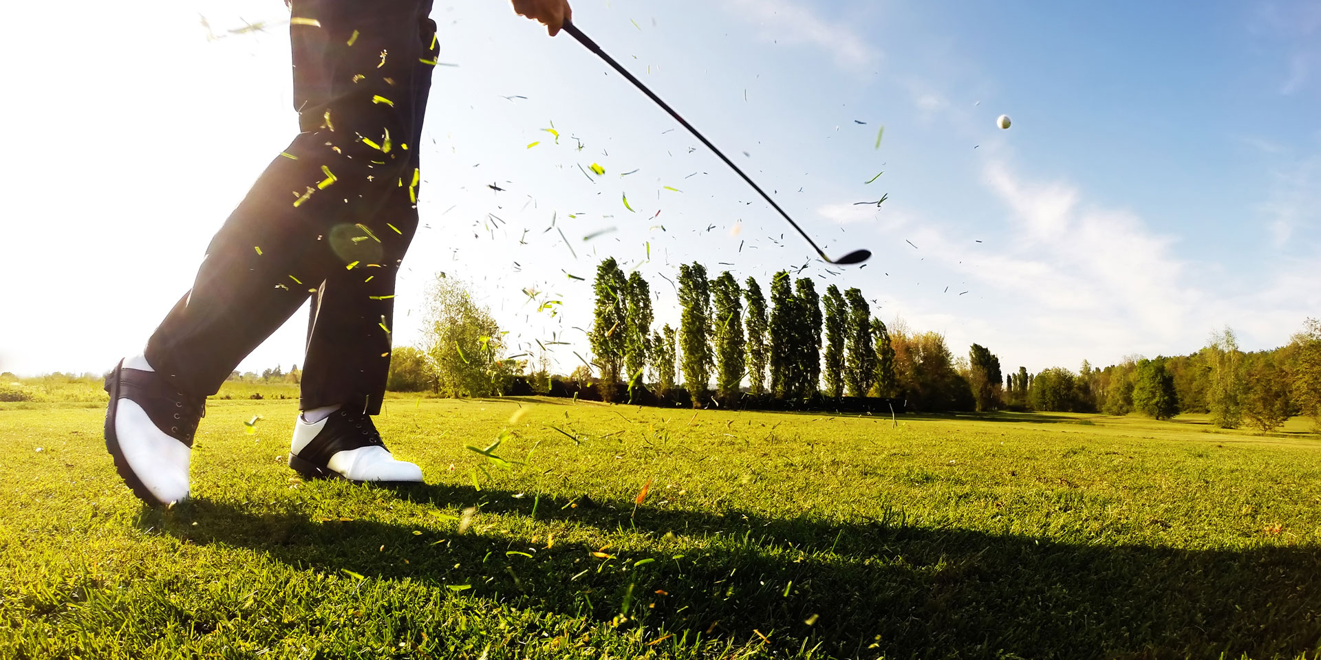 Golfer teeing off with tall cypress trees in the background
