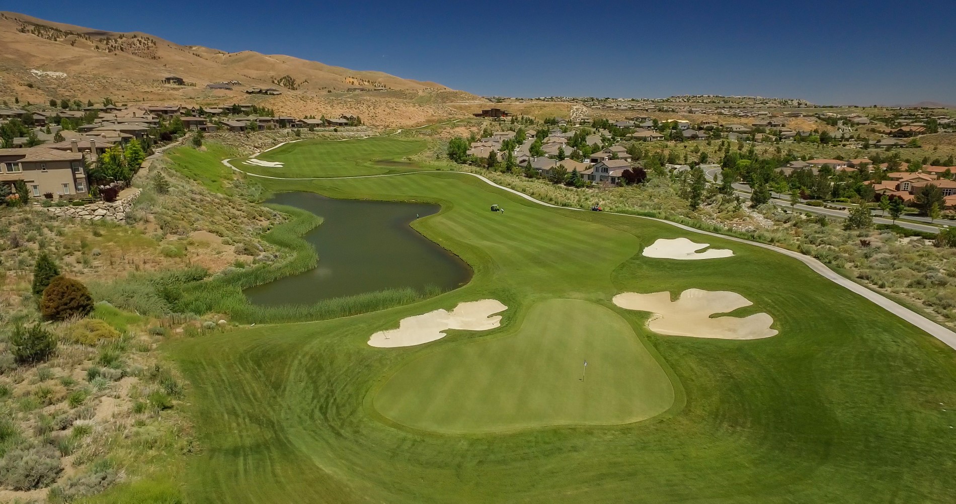 Green in the foreground with 3 sand traps and a water hazard bordering the approaching fairway
