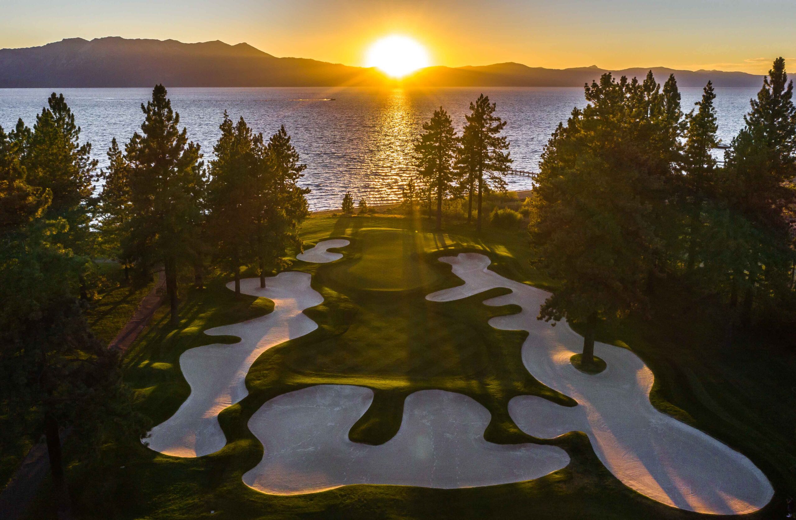 Sand bunkers surrounding a tree-lined green with a lake just beyond